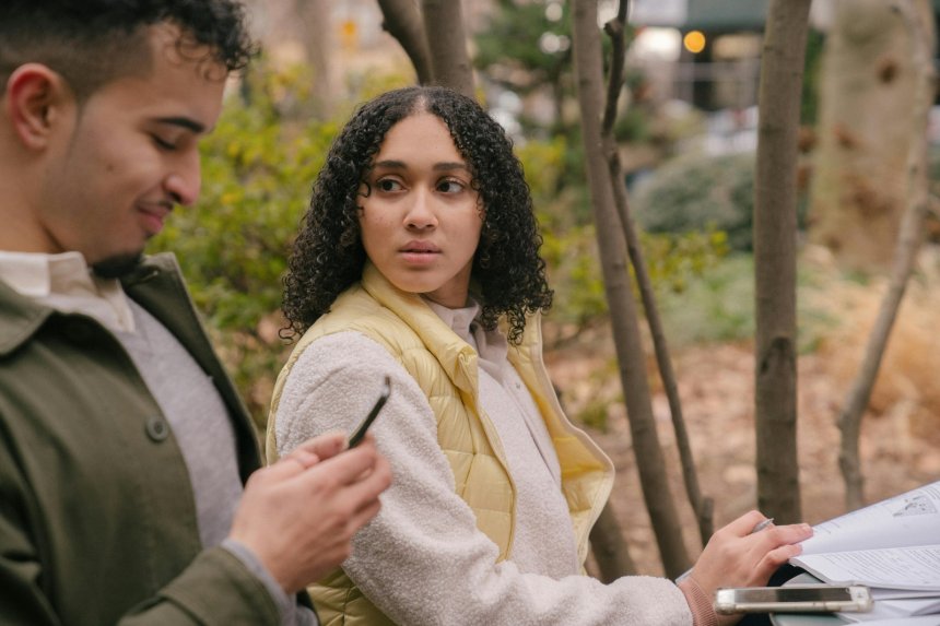 smiling man checking his phone while his girlfriend observes