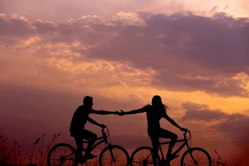 man and woman cycling together into the sunset